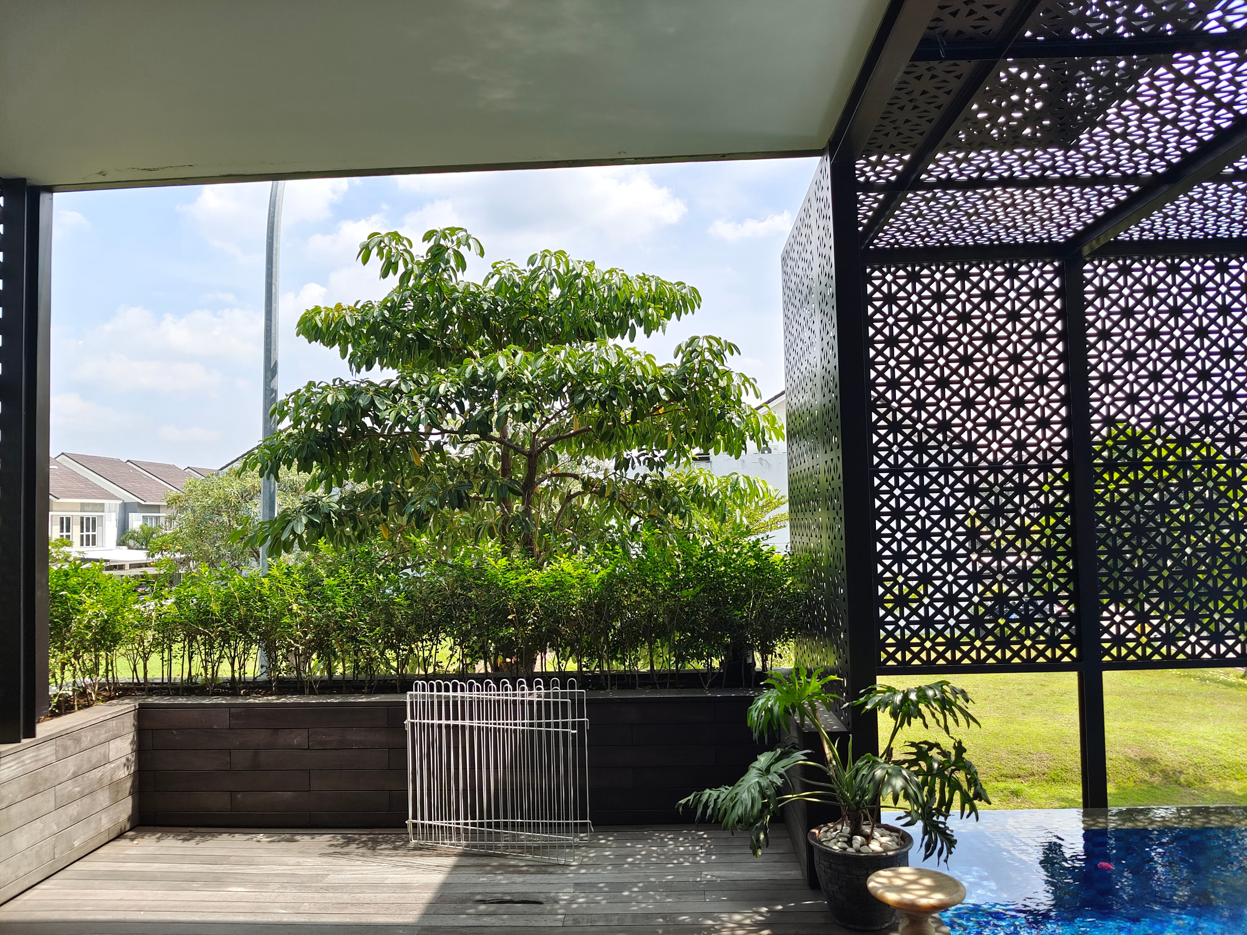 Pool terrace hardwood decking viewed through sliding door with timber-clad planter box border at JGC residence by Reywood Indonesia