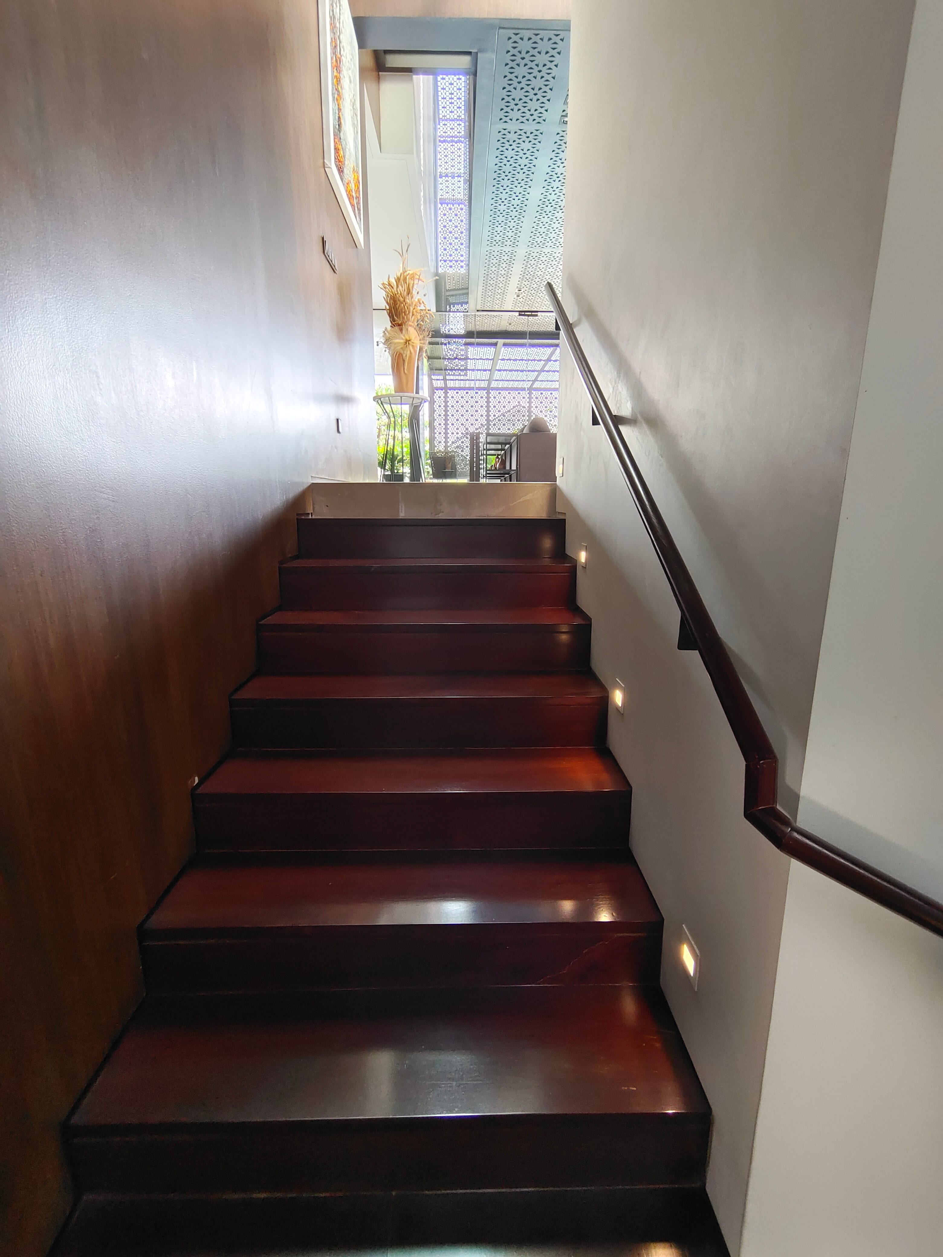 Solid wood staircase from below looking up, showing dark hardwood treads with step lights and solid wood wall cladding on the left at JGC by Reywood